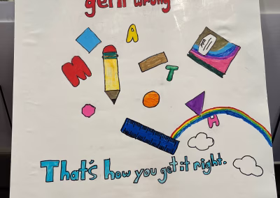 A colorful poster with the phrase “Don’t be afraid to get it wrong. MATH. That’s how you get it right.” Illustrated with math objects like a ruler, pencil, and book, plus a rainbow and clouds.