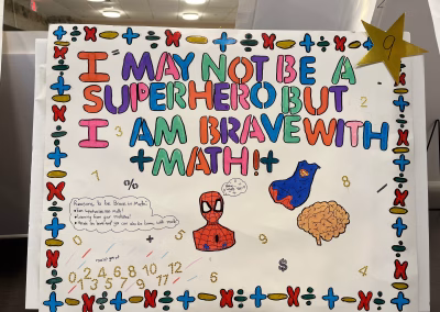 A colorful poster reads, I may not be a superhero but I am brave with math! with superhero drawings, math symbols, and a list of reasons to be brave in math. A gold star with the number 9 is in the upper right corner.